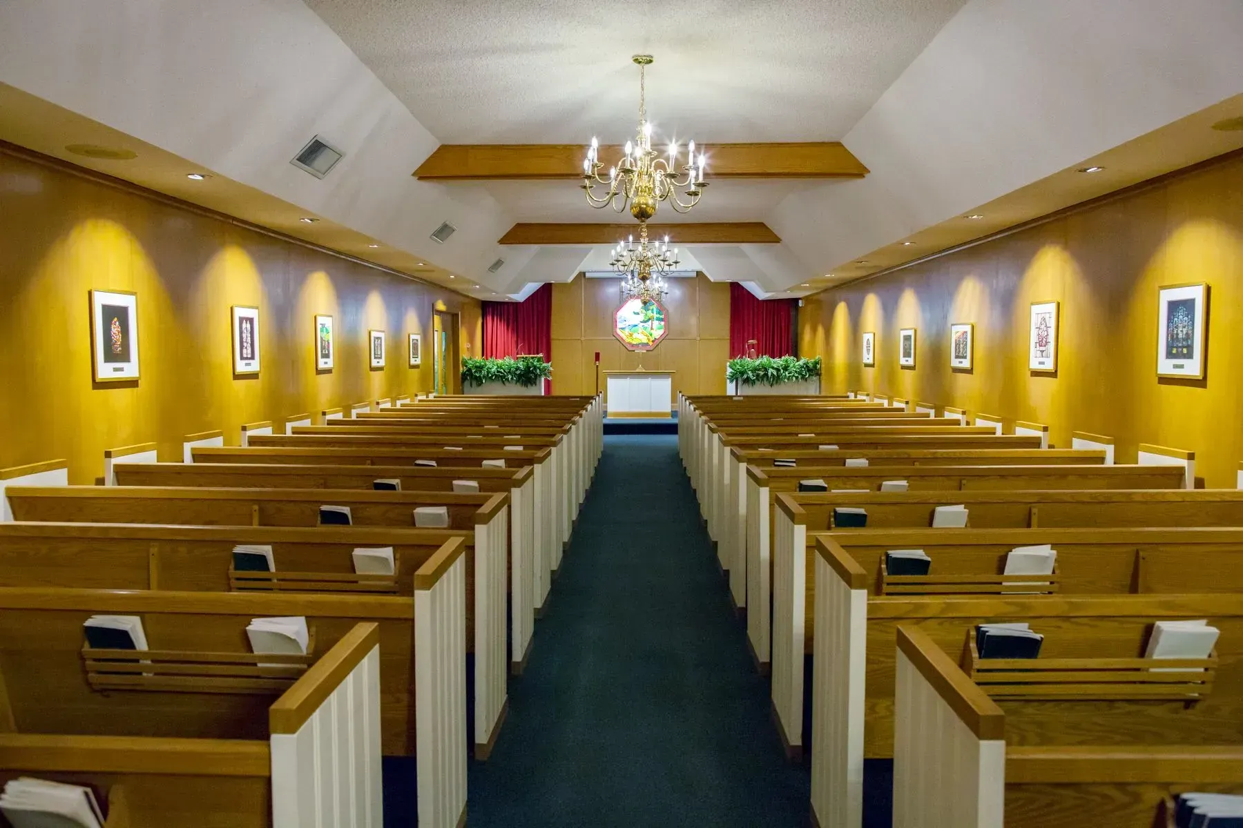 Empty chapel interior with wooden pews, yellow walls, and a central aisle leading to the altar