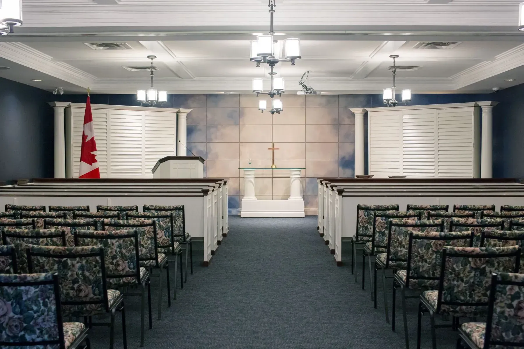 Small chapel with rows of pews, white altar, Canadian flag, and bright ceiling lights in a formal room