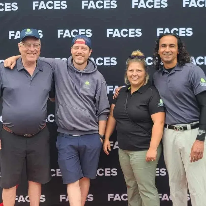 Four people posing in front of a “FACES” backdrop at an event, smiling and standing side by side