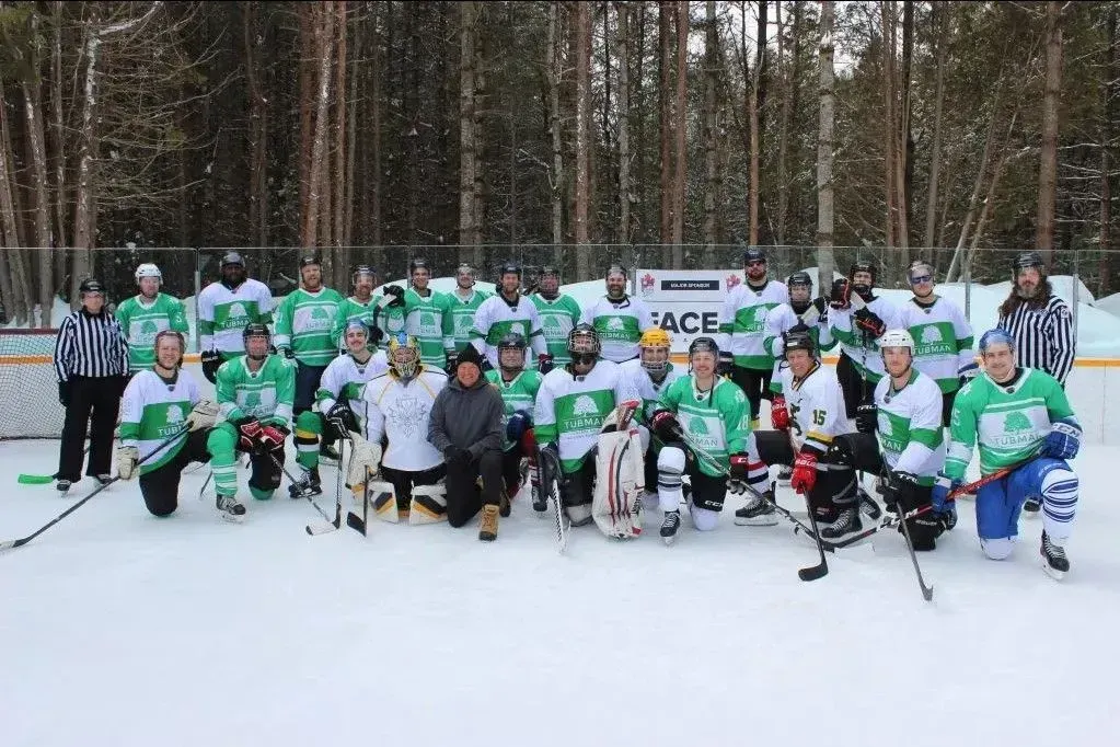 Hockey team posing on an outdoor ice rink in snowy woods, wearing green and white jerseys