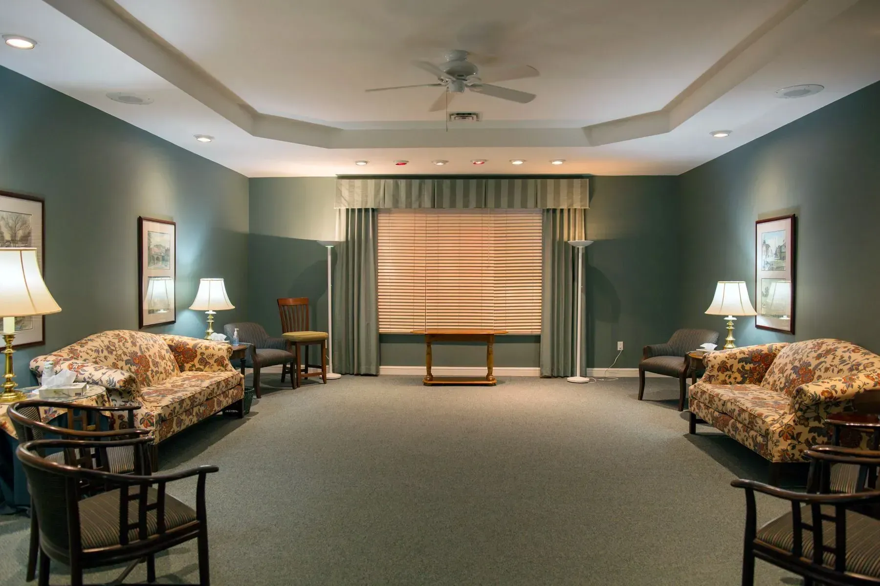 Symmetrical living room with sofas, lamps, and a large window with blinds in the center.