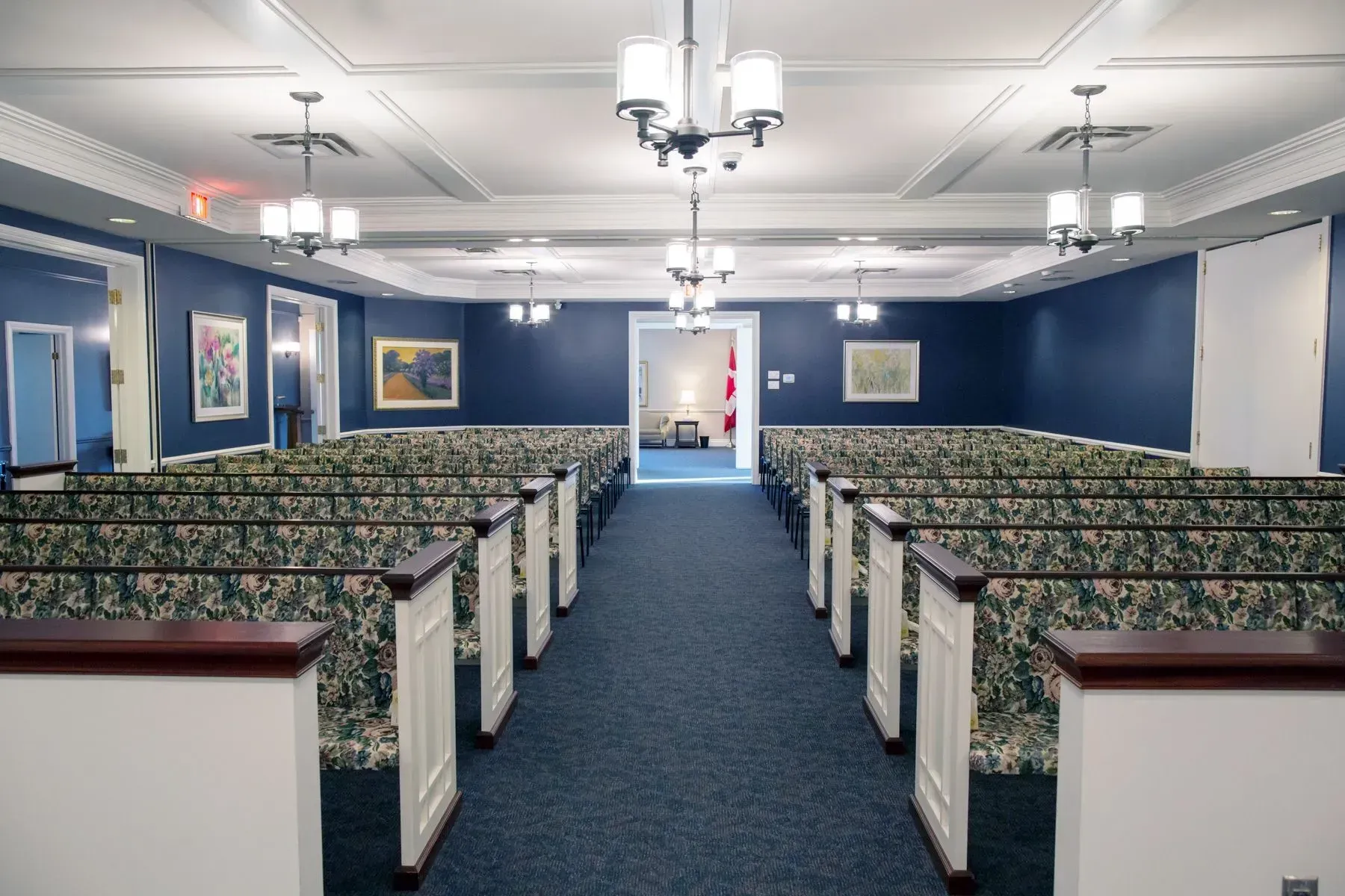Empty church sanctuary with blue carpet, pews, chandeliers, and framed wall art