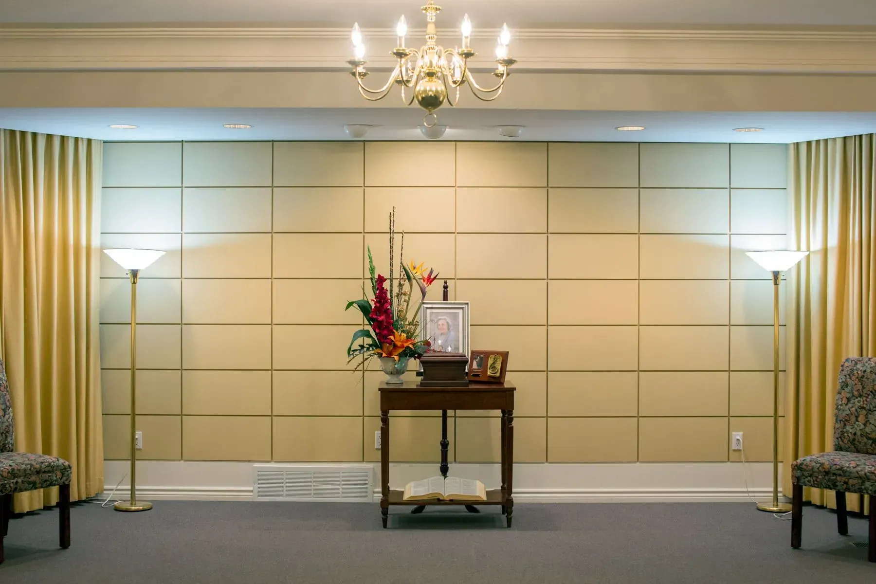 Elegant lobby with chandelier, wall lamps, central floral arrangement, and seating along the sides