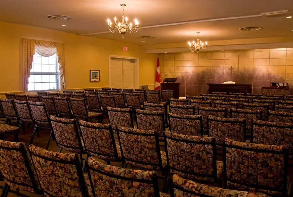 Empty banquet hall with rows of patterned chairs, chandeliers, and a small stage at the front