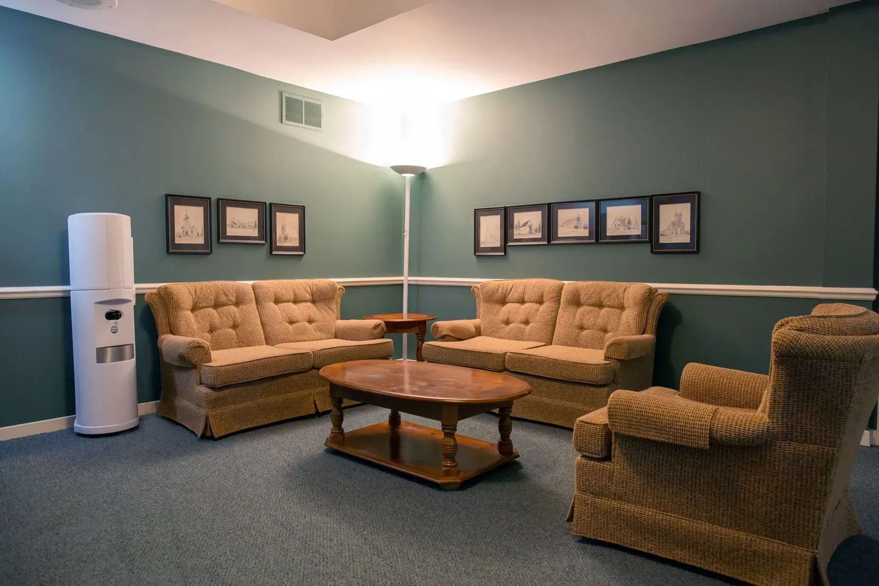 Waiting area with teal walls, beige sofas, armchairs, a coffee table, and framed art