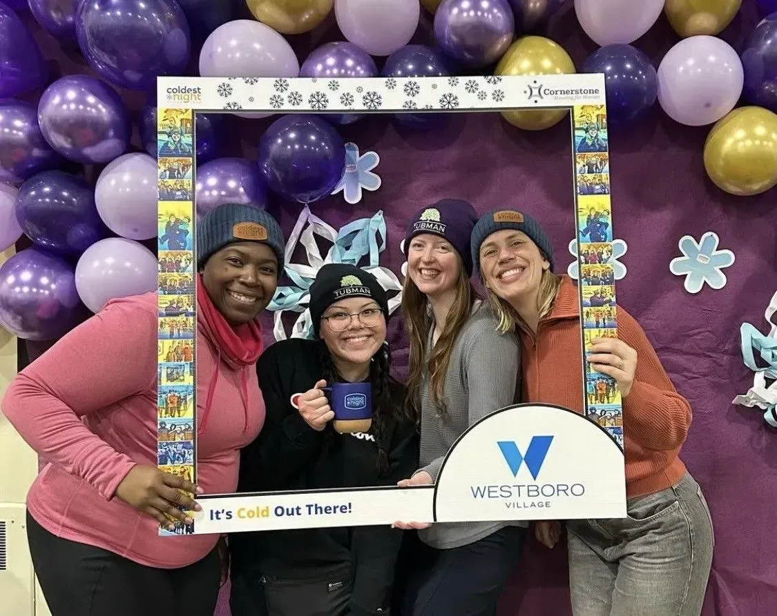 Four people posing in a purple balloon backdrop holding a Wildfire-branded frame and mug, smiling.