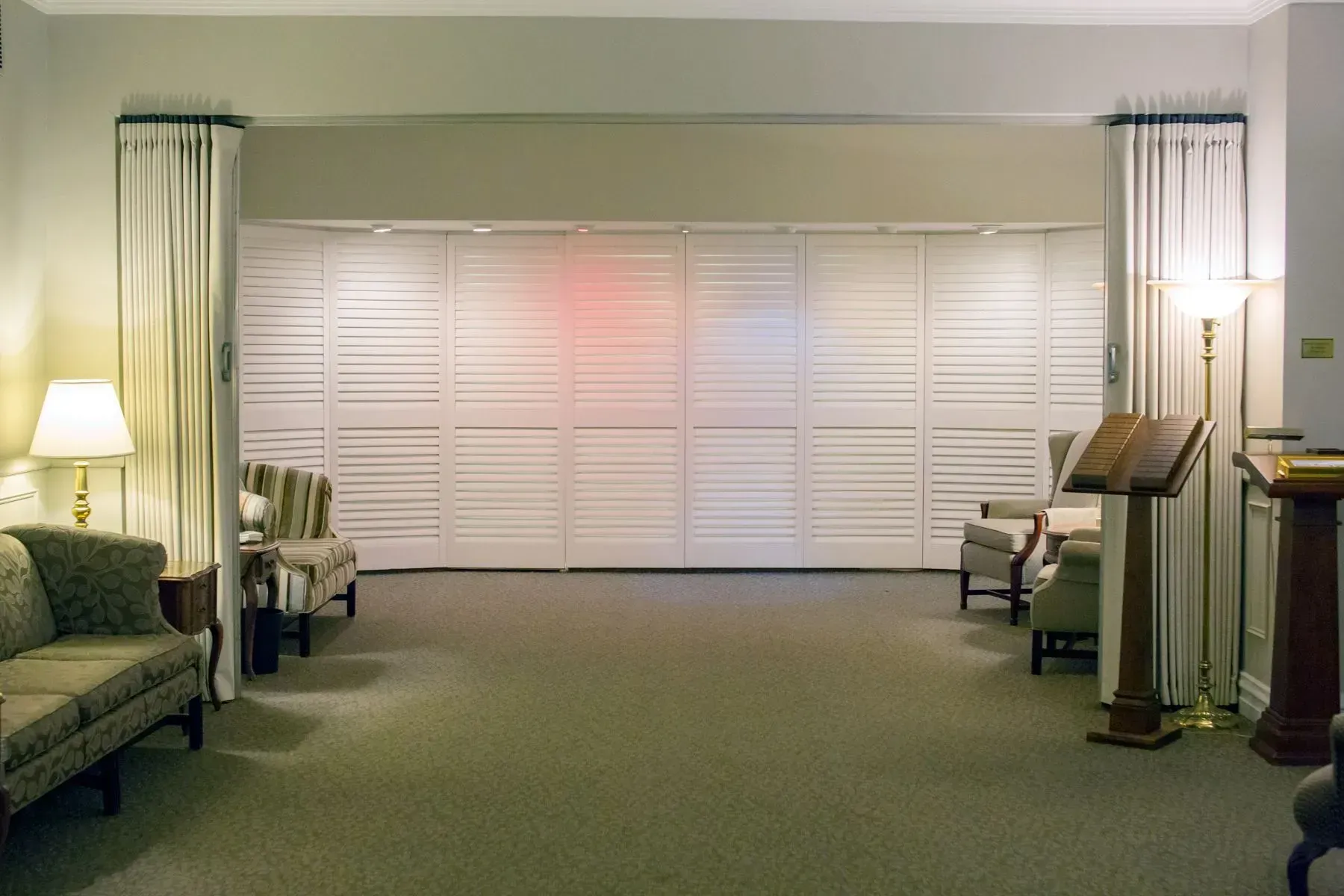 Living room with white shutters, green carpet, sofas, lamps, and small tables