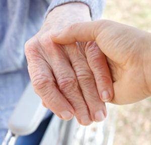 Two hands gently clasping in a caring gesture, one older and one younger, with soft outdoor light