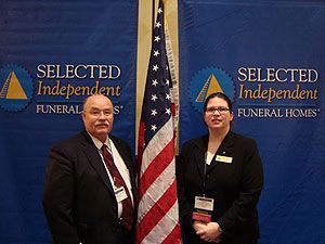Two people standing beside a U.S. flag at a Selected Independent Funeral Homes event booth