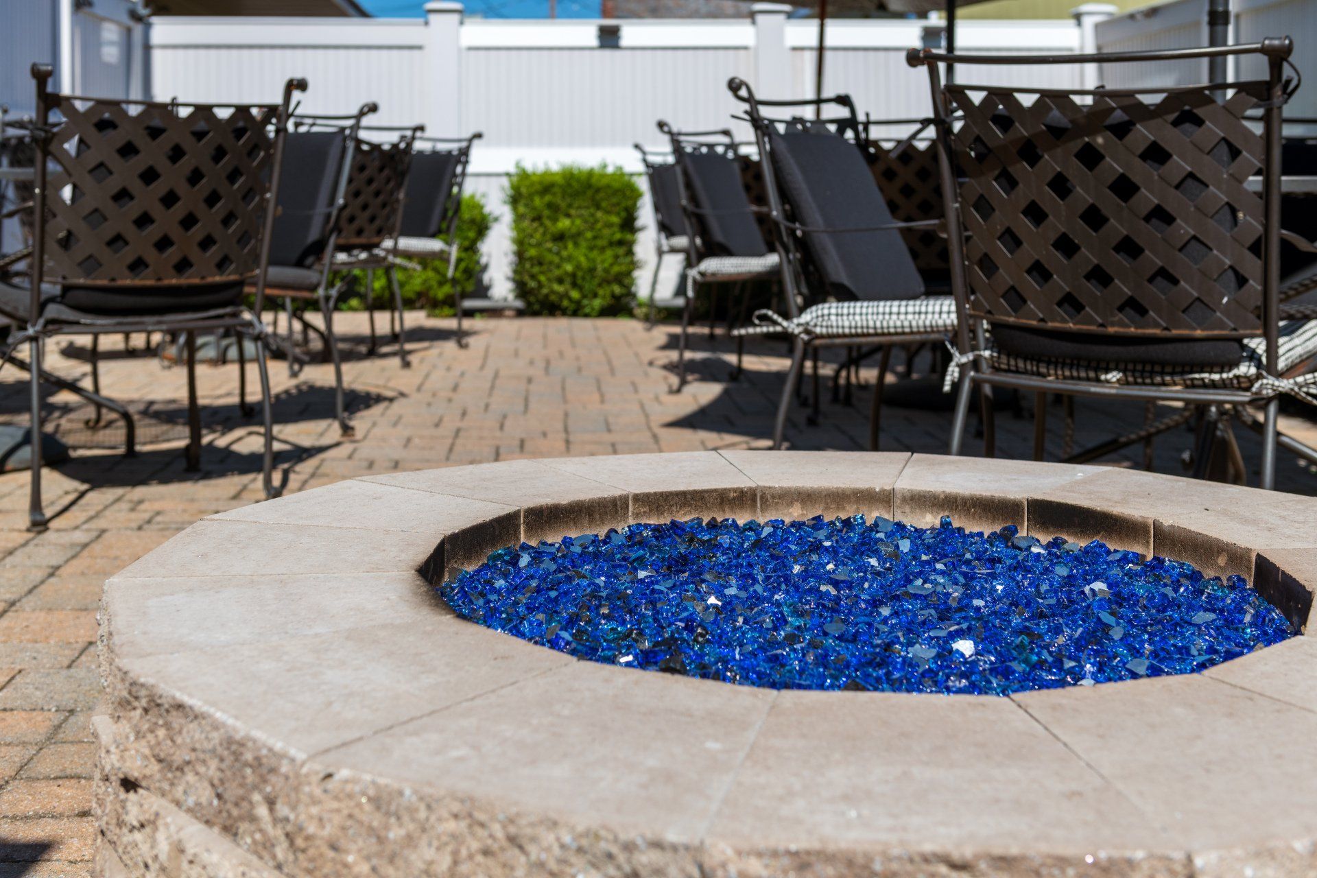 A fire pit filled with blue glass on a patio with chairs.