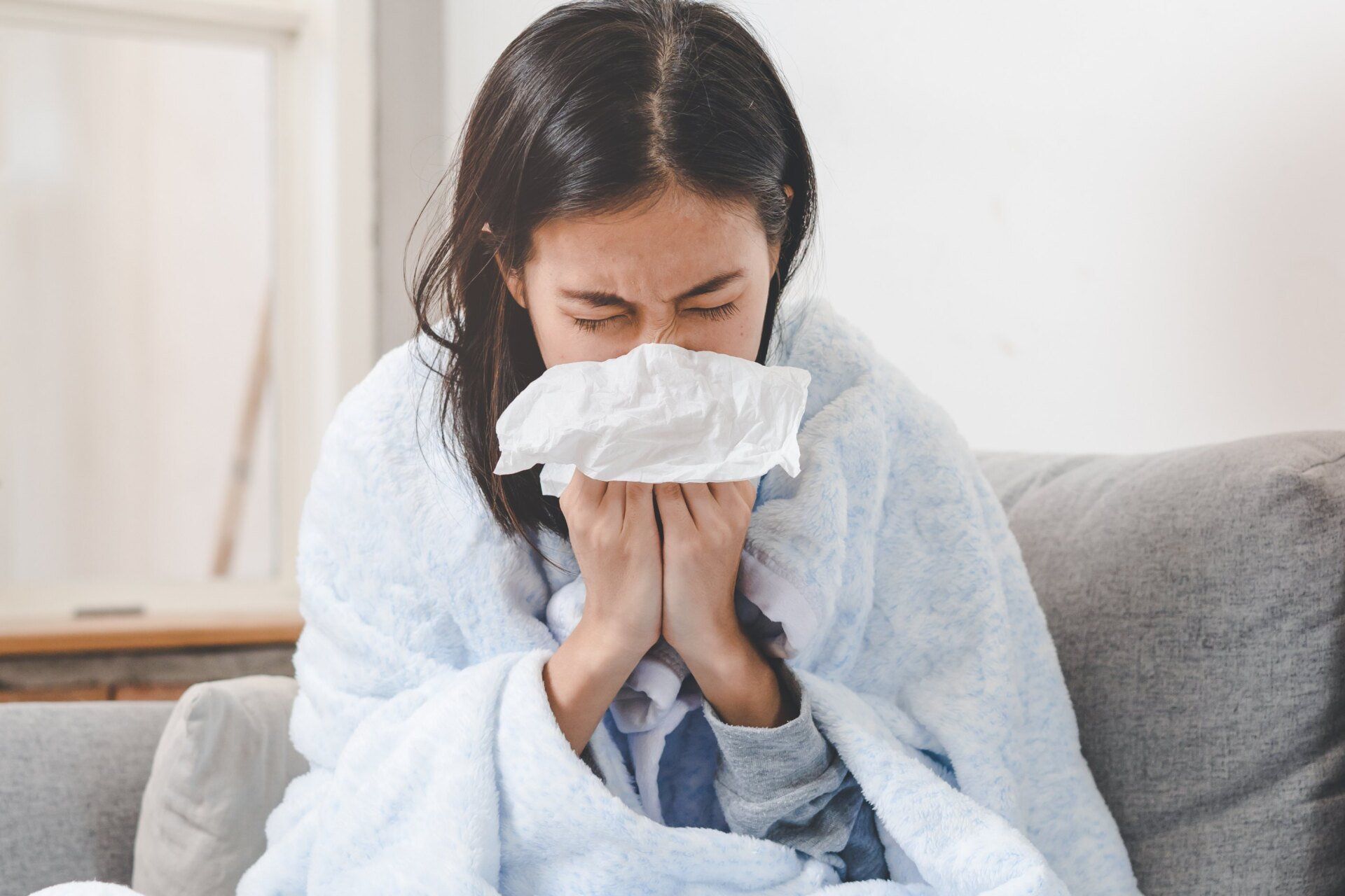 sick young asian woman blowing nose into tissue