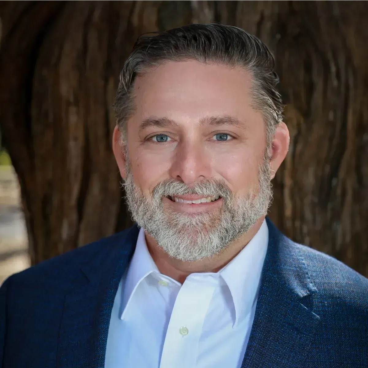 A man with a beard is wearing a suit and smiling for the camera.