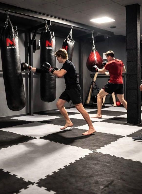 Twee mensen trainen in een bokszaal met bokszakken en zwart-witte matten.