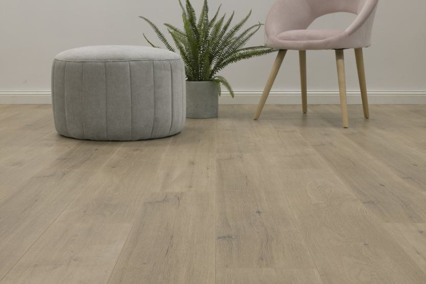 A Chair and Ottoman are Sitting on a Wooden Floor Next to a potted plant — Flooring Suppliers in Port Macquarie, NSW.