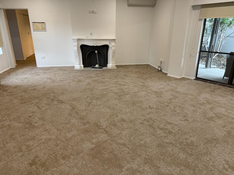 Empty room with tan carpet, a white fireplace mantle, a doorway on the left, and a large sliding glass door on the right.