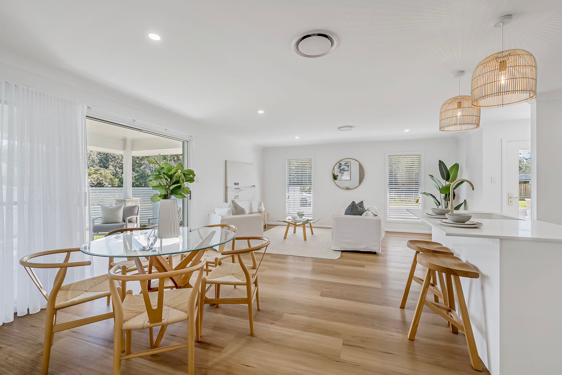 Bright modern dining and living room with light wood floors, white walls, and wicker chairs by large windows