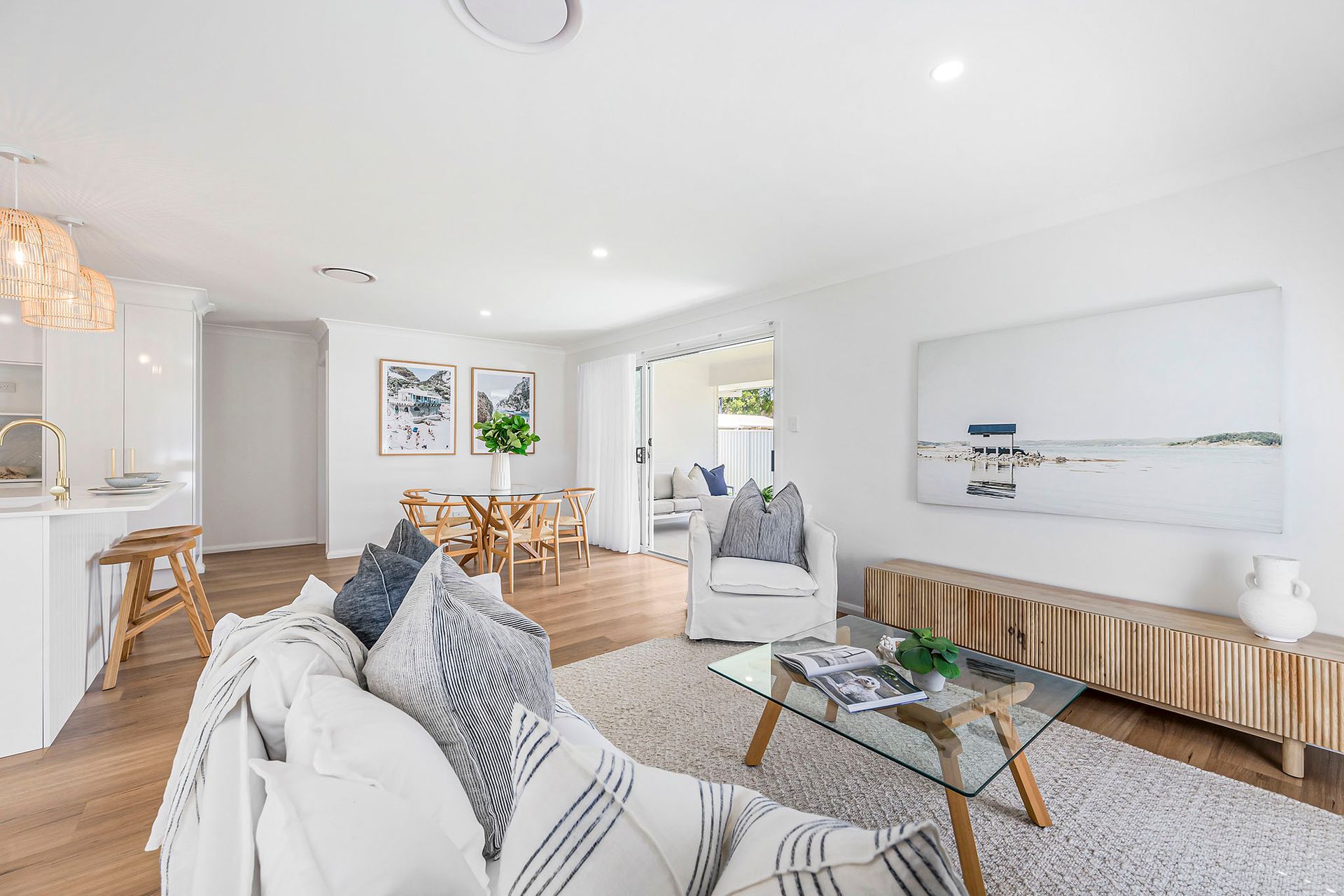 Bright white living room with sofa, glass coffee table, wall art, and dining area in the background