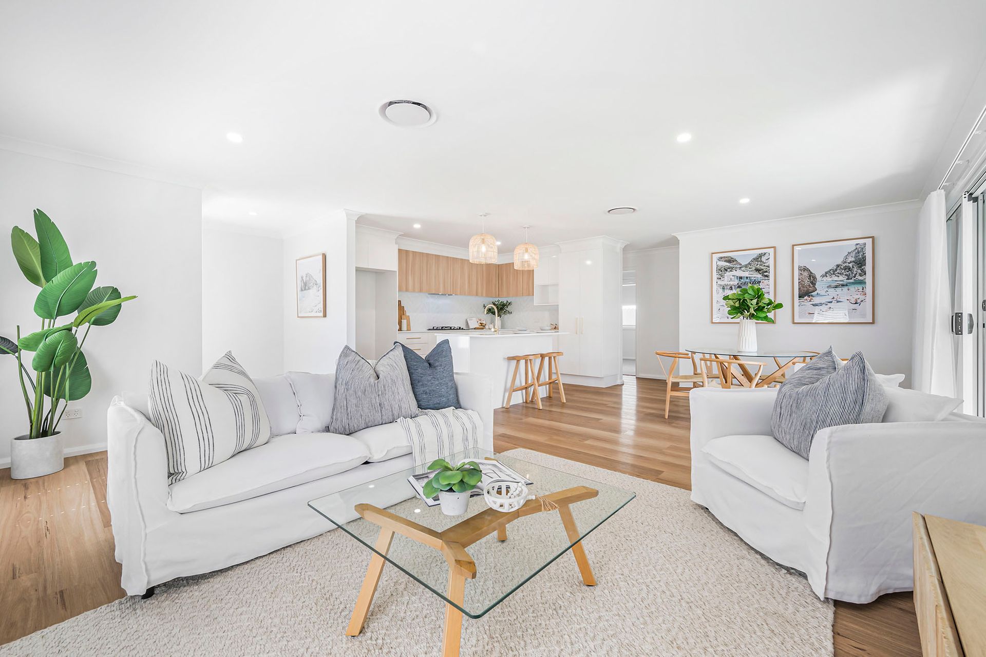 Bright modern living room with white sofas, wood floors, and an open kitchen in the background