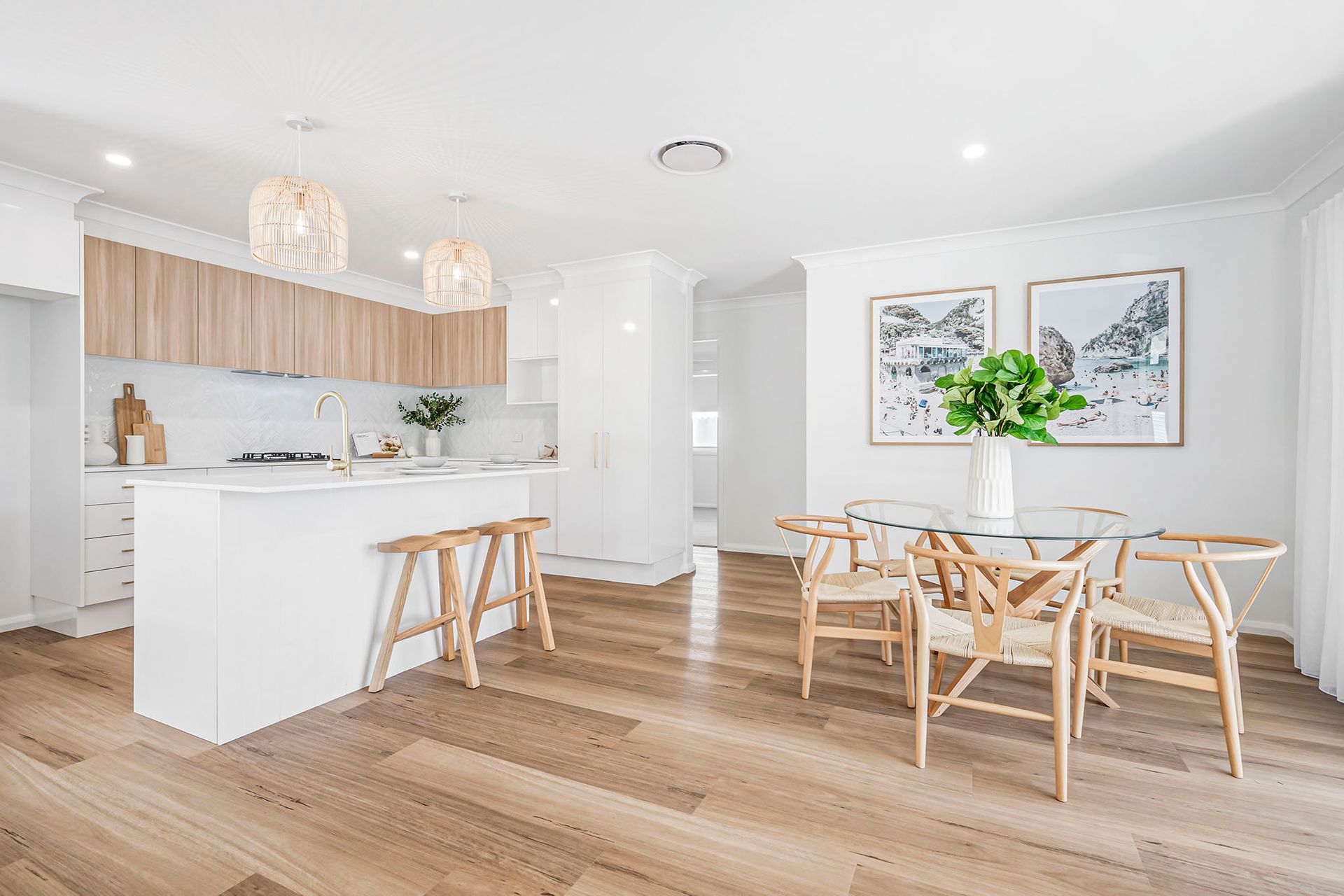 Bright modern kitchen and dining area with white cabinets, wood floors, and a round table by framed wall art