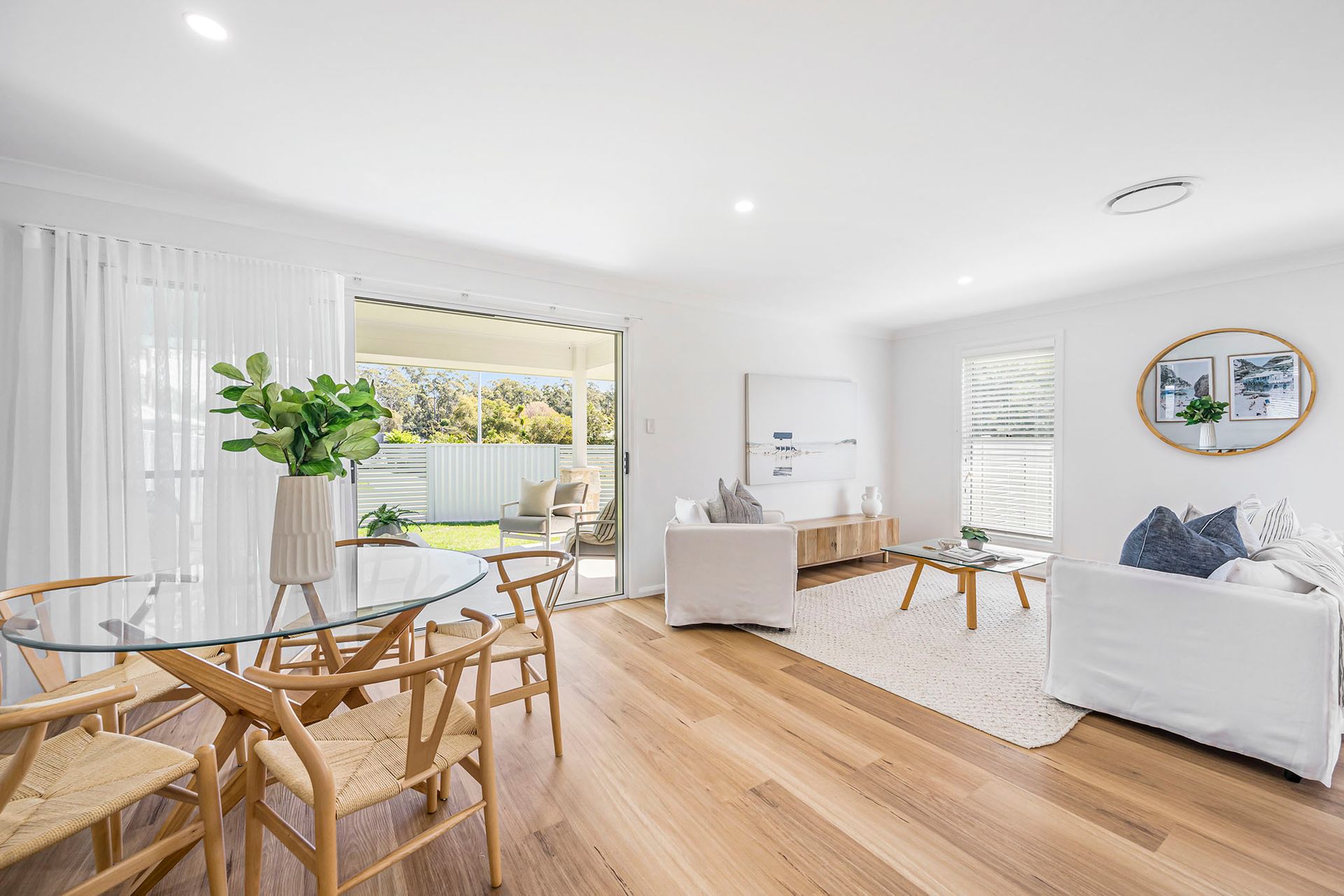 Bright open living room with wood floors, white walls, dining table, sofa, and large window view