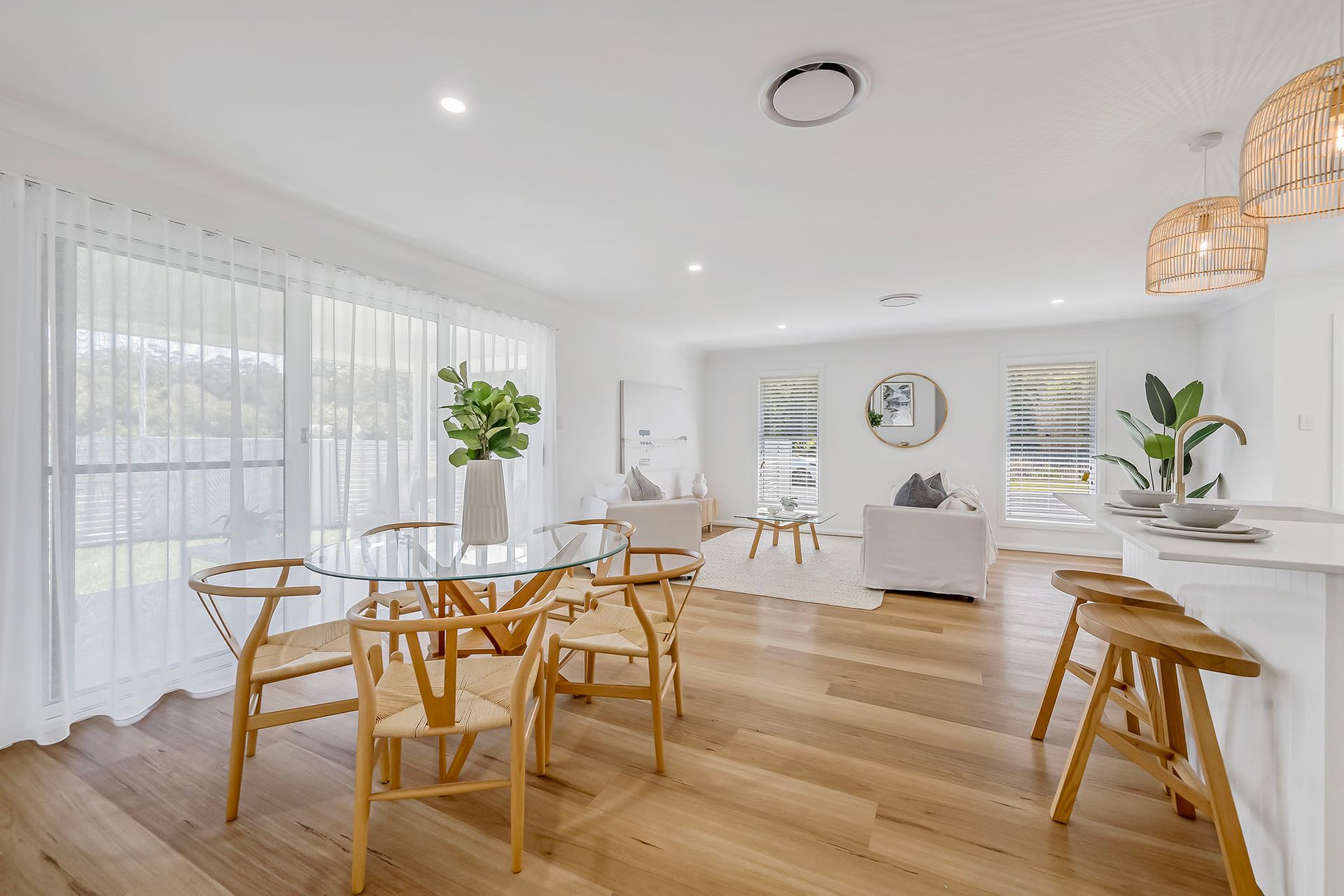 Bright minimalist dining room with wooden chairs, white walls, and large windows with sheer curtains.