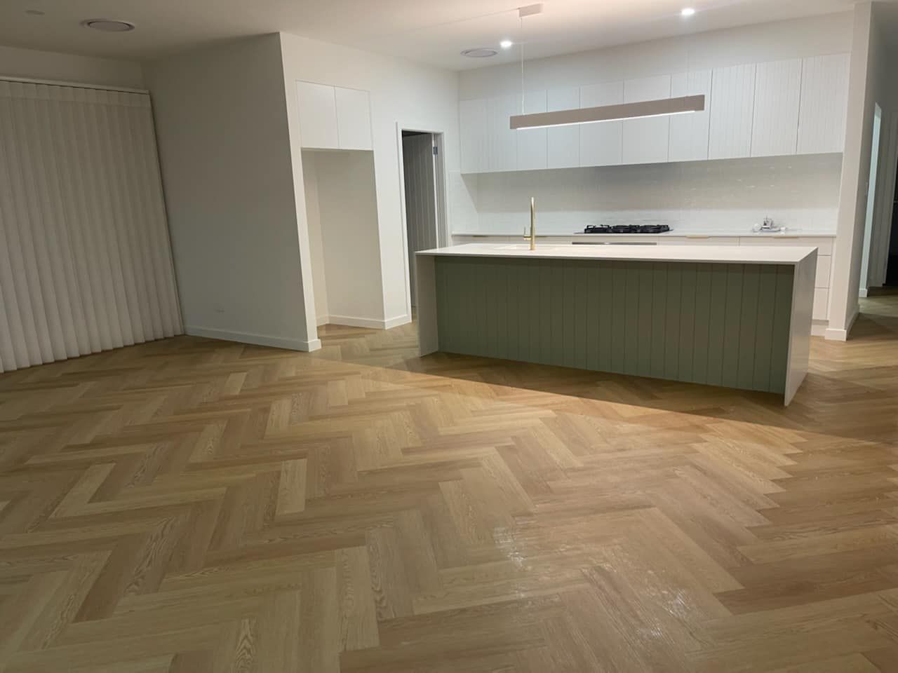 A modern kitchen featuring light wood herringbone floors, a sage green kitchen island, and white cabinetry.