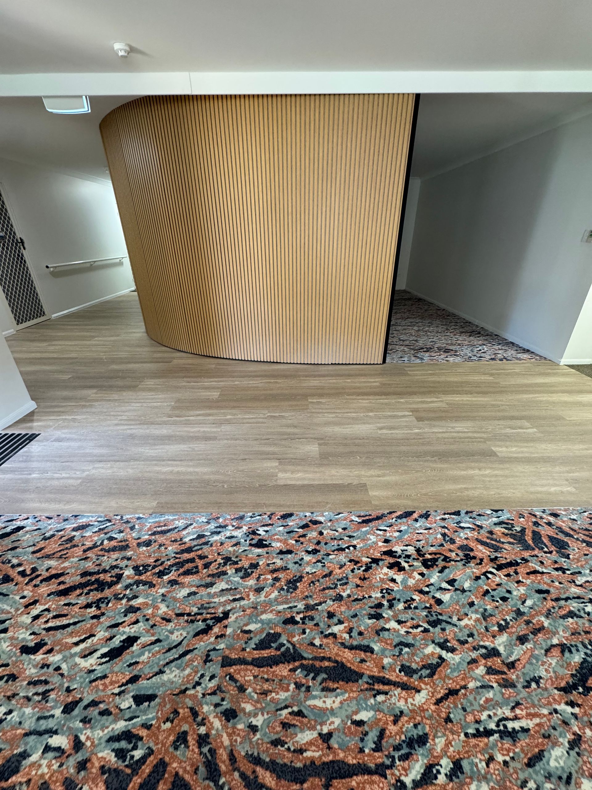 Modern interior hallway with patterned carpet, wood floor, and a curved wooden wall panel
