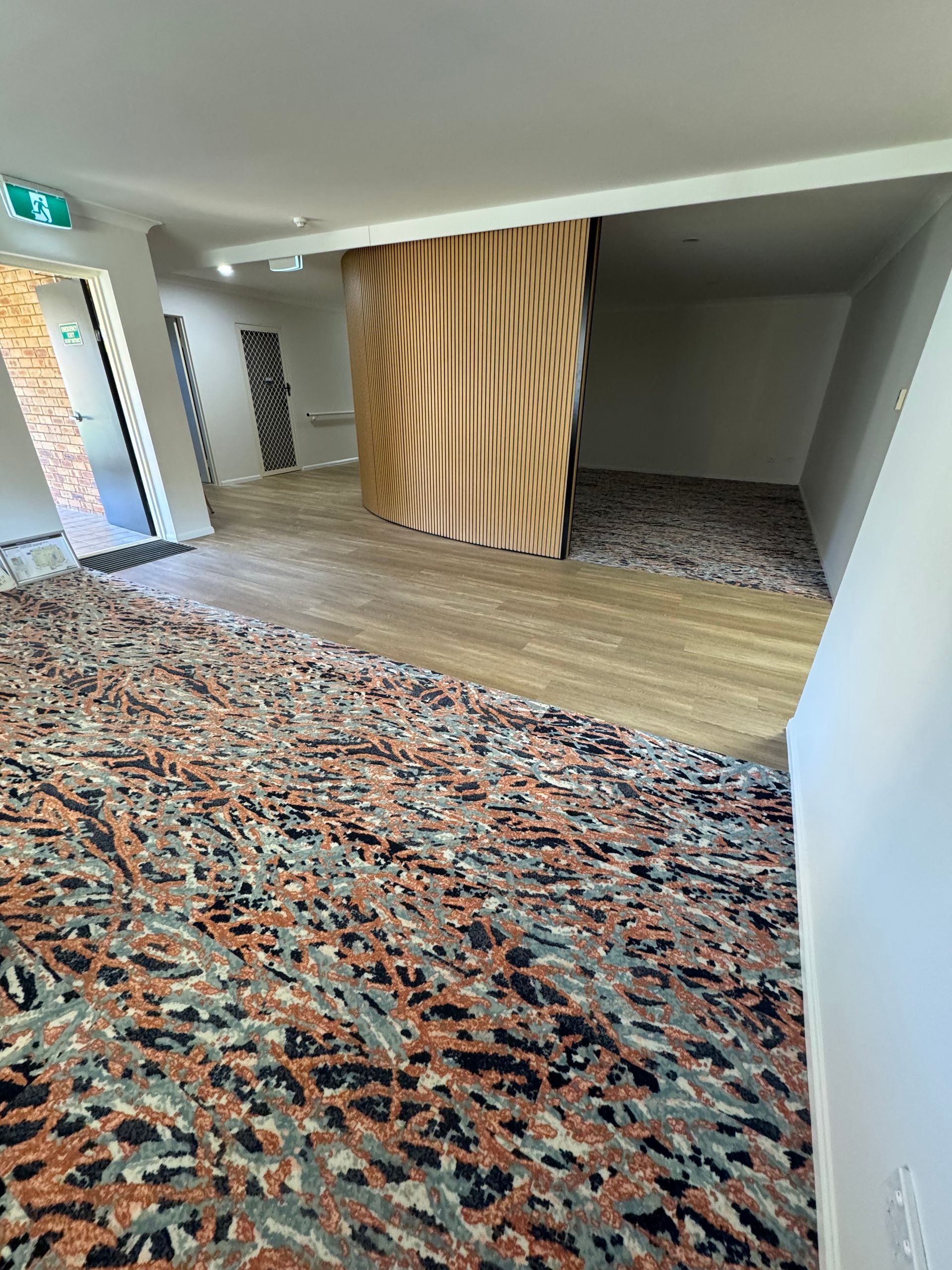 Empty room with patterned carpet, light wood floor, and a wood-paneled wall divider