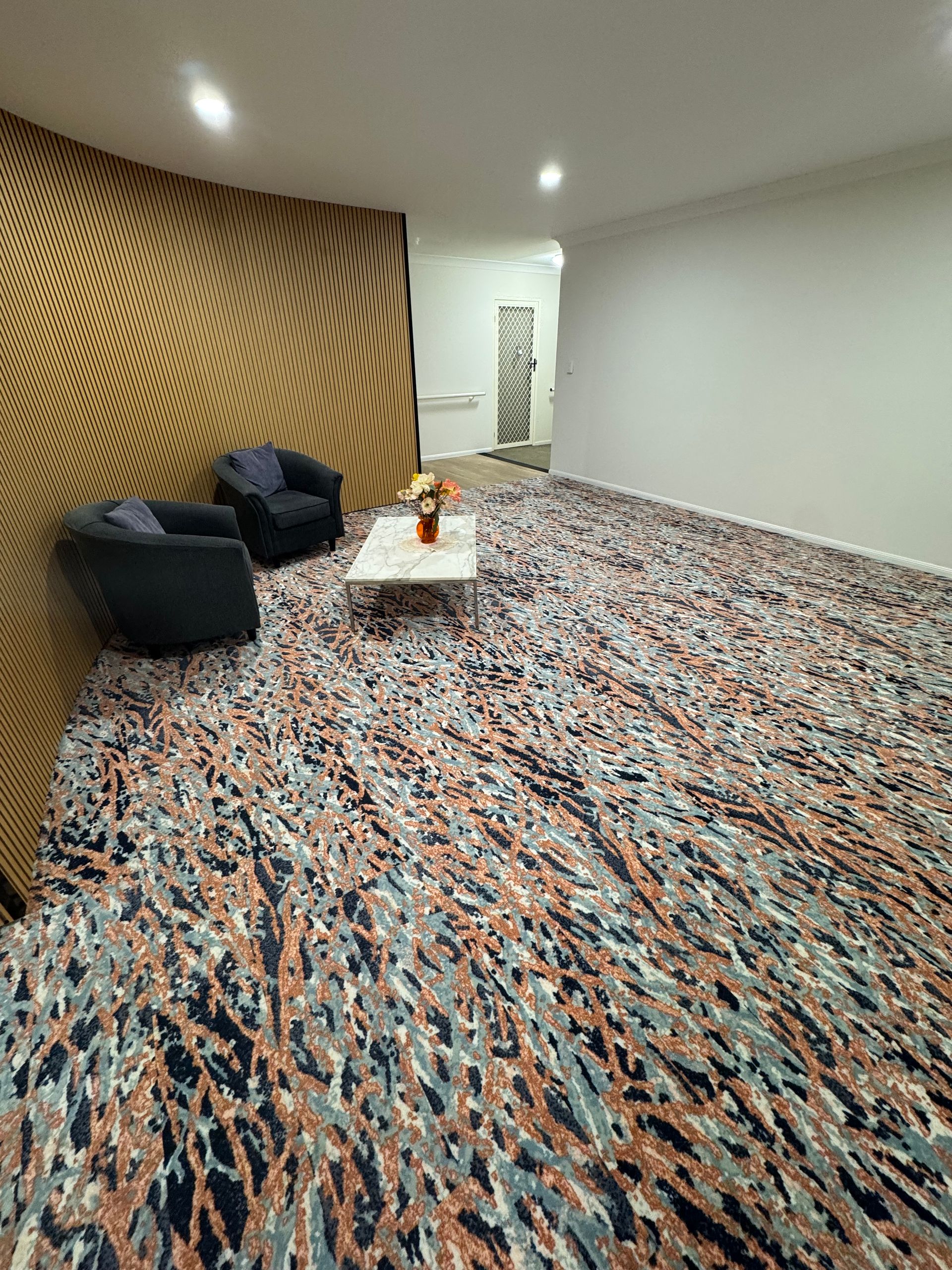 Modern lounge with patterned carpet, black chairs, wood slat wall, and white ceiling lights