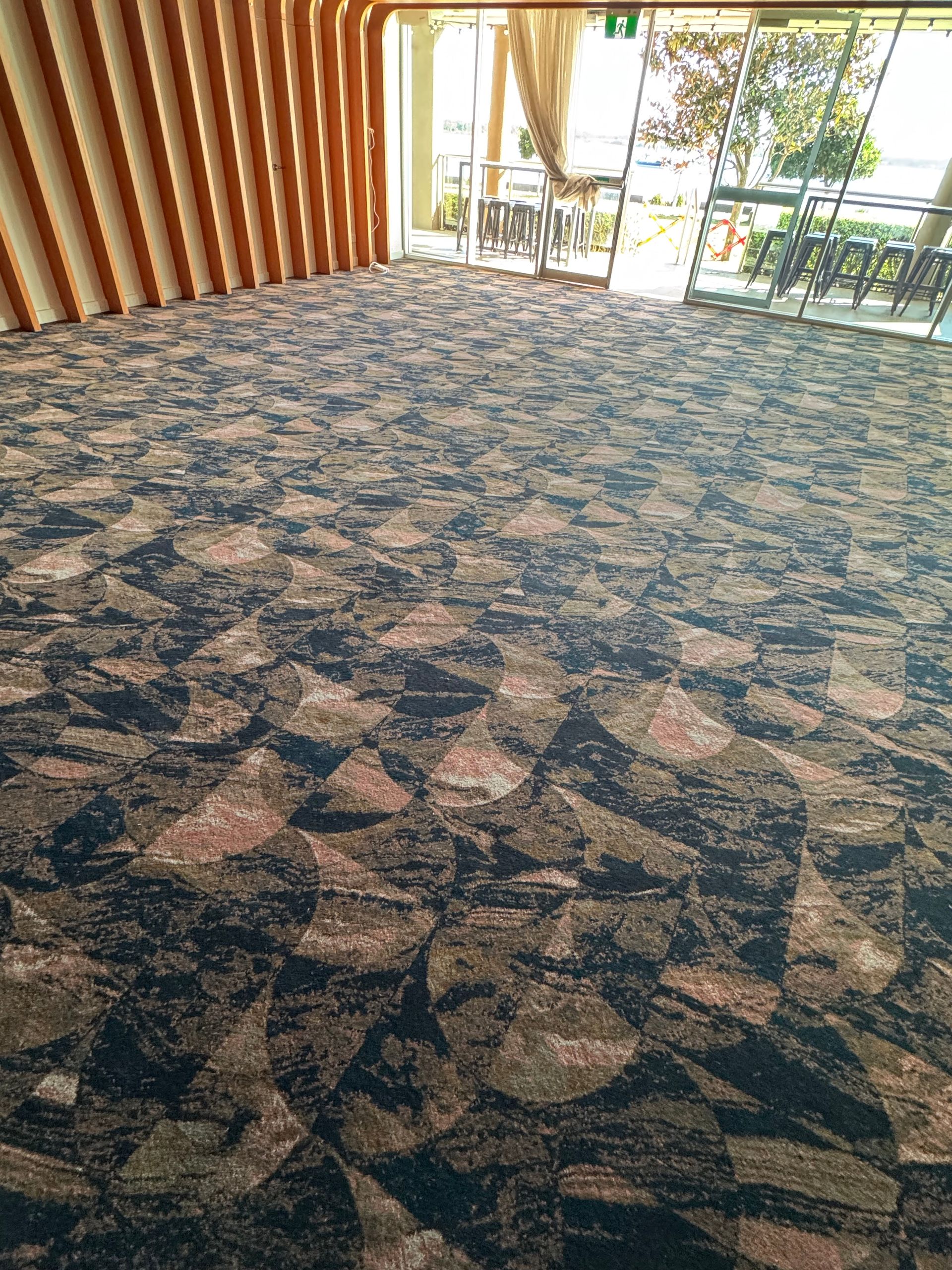 Patterned blue carpet in a bright lobby with glass doors and wooden wall panels
