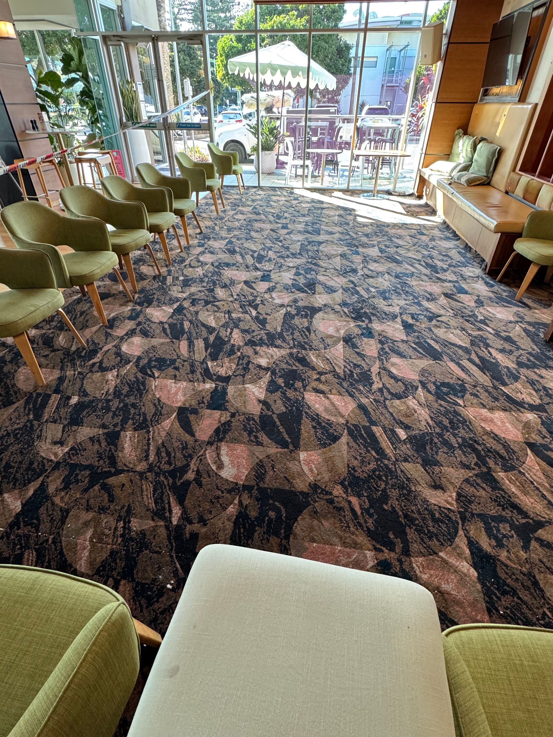 Modern lounge with green chairs, patterned carpet, and bright windows at the far end