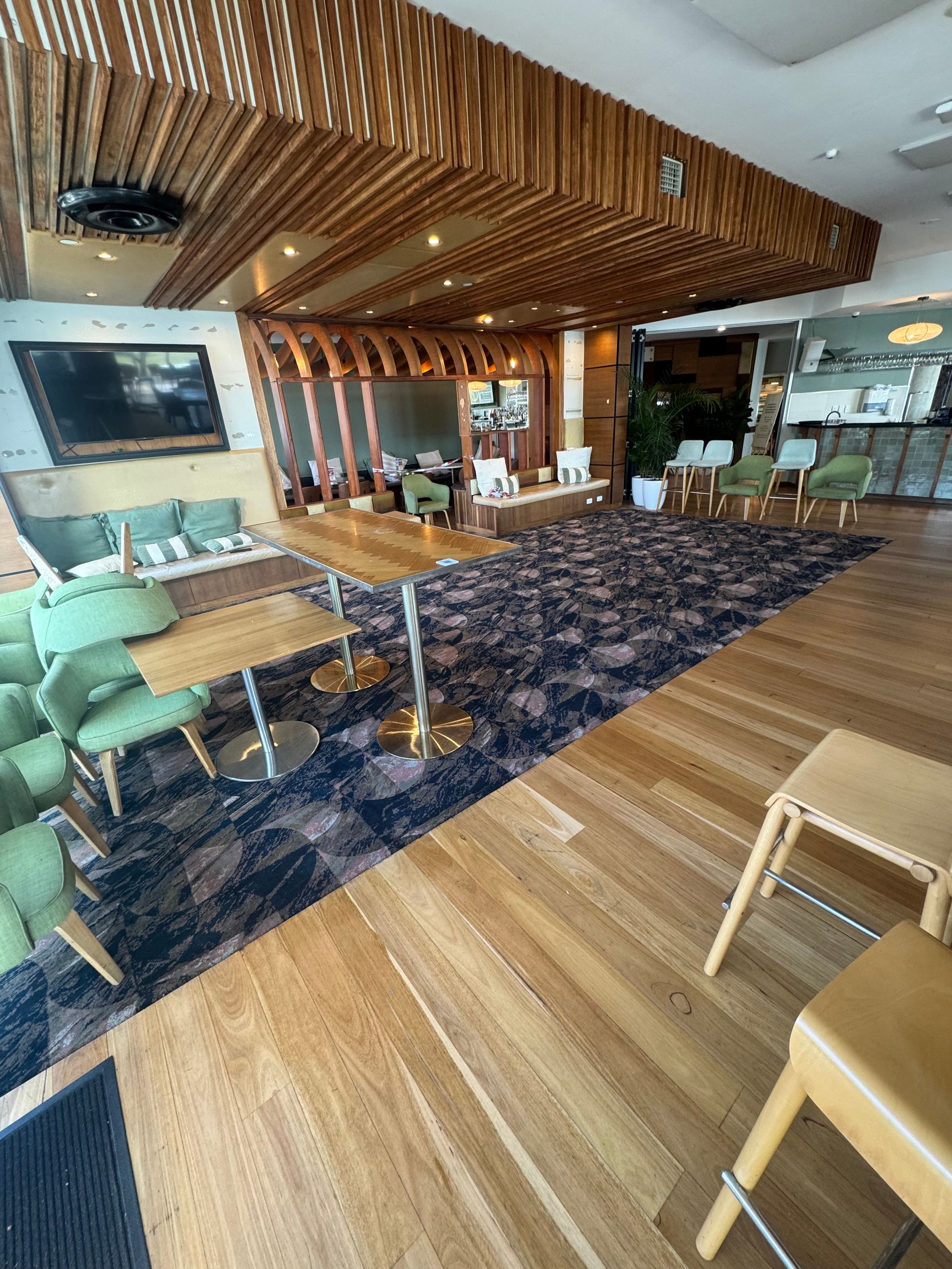 Modern lounge with wood ceiling, green chairs, bar counter, and patterned carpet indoors
