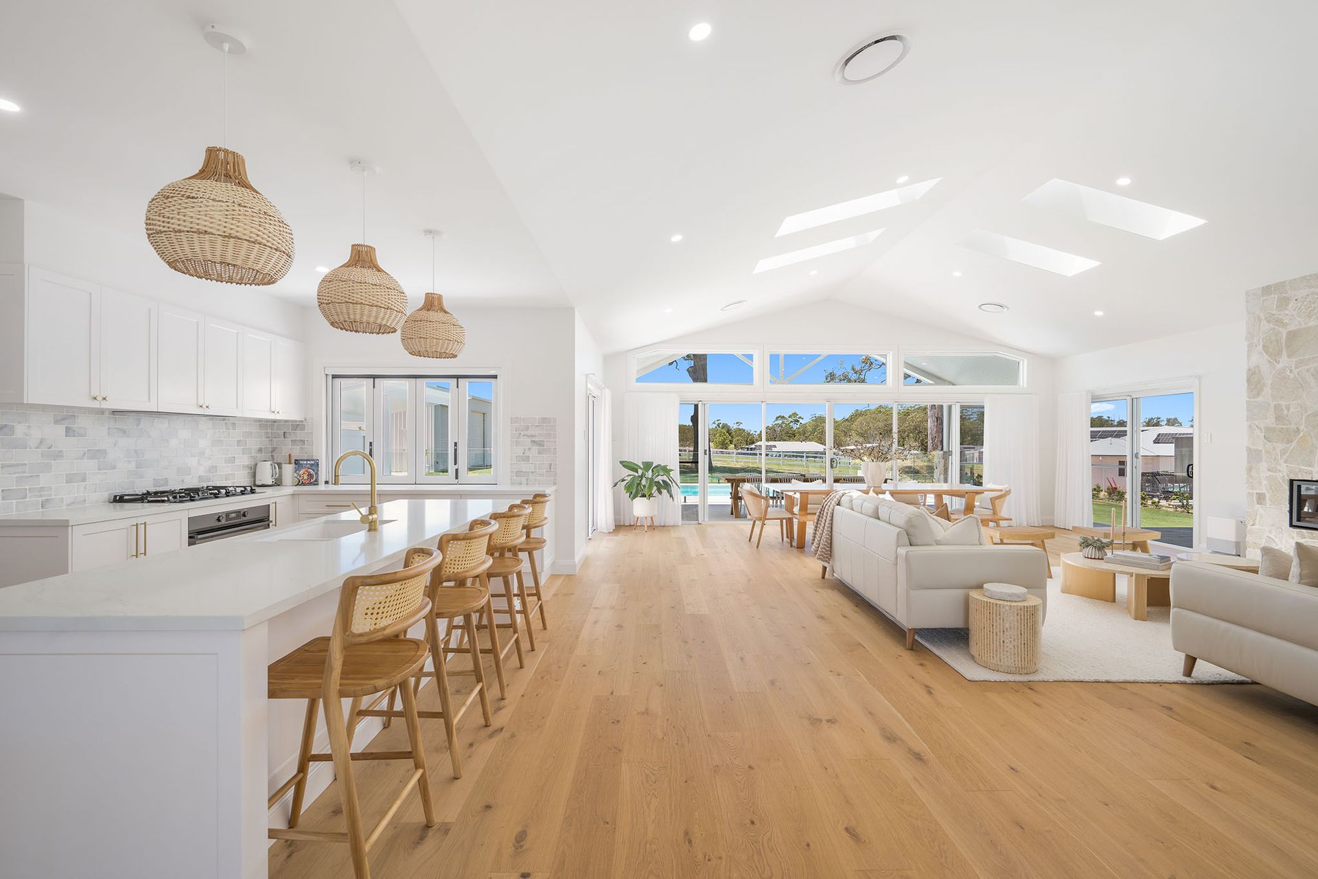 Bright open-plan living room and kitchen with white walls, wood floors, wicker pendant lights, and ocean views
