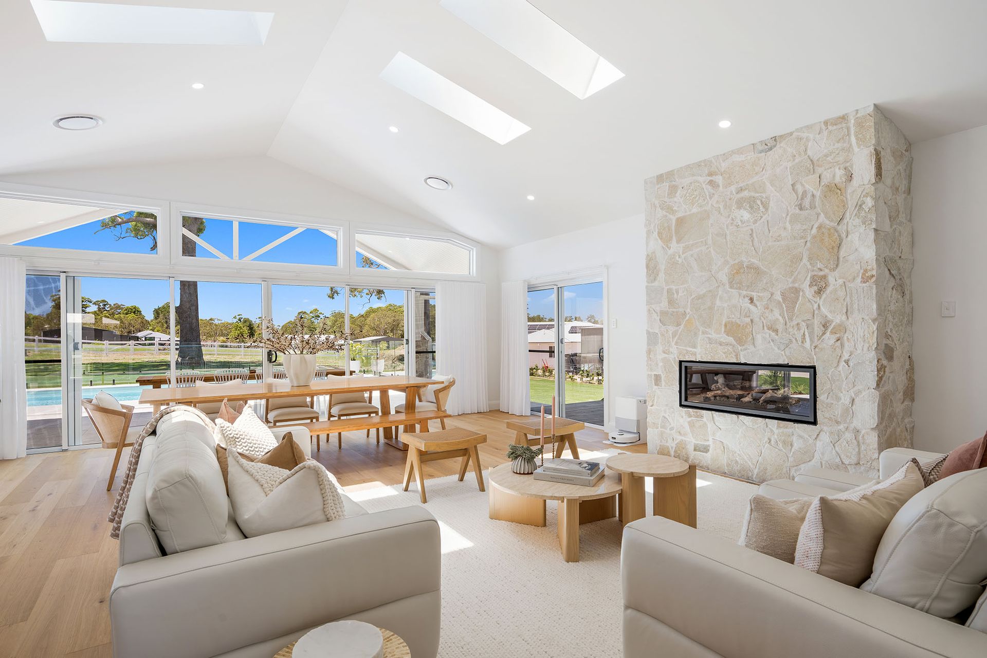 Bright modern living room with white sofas, stone fireplace, large windows, and an ocean view