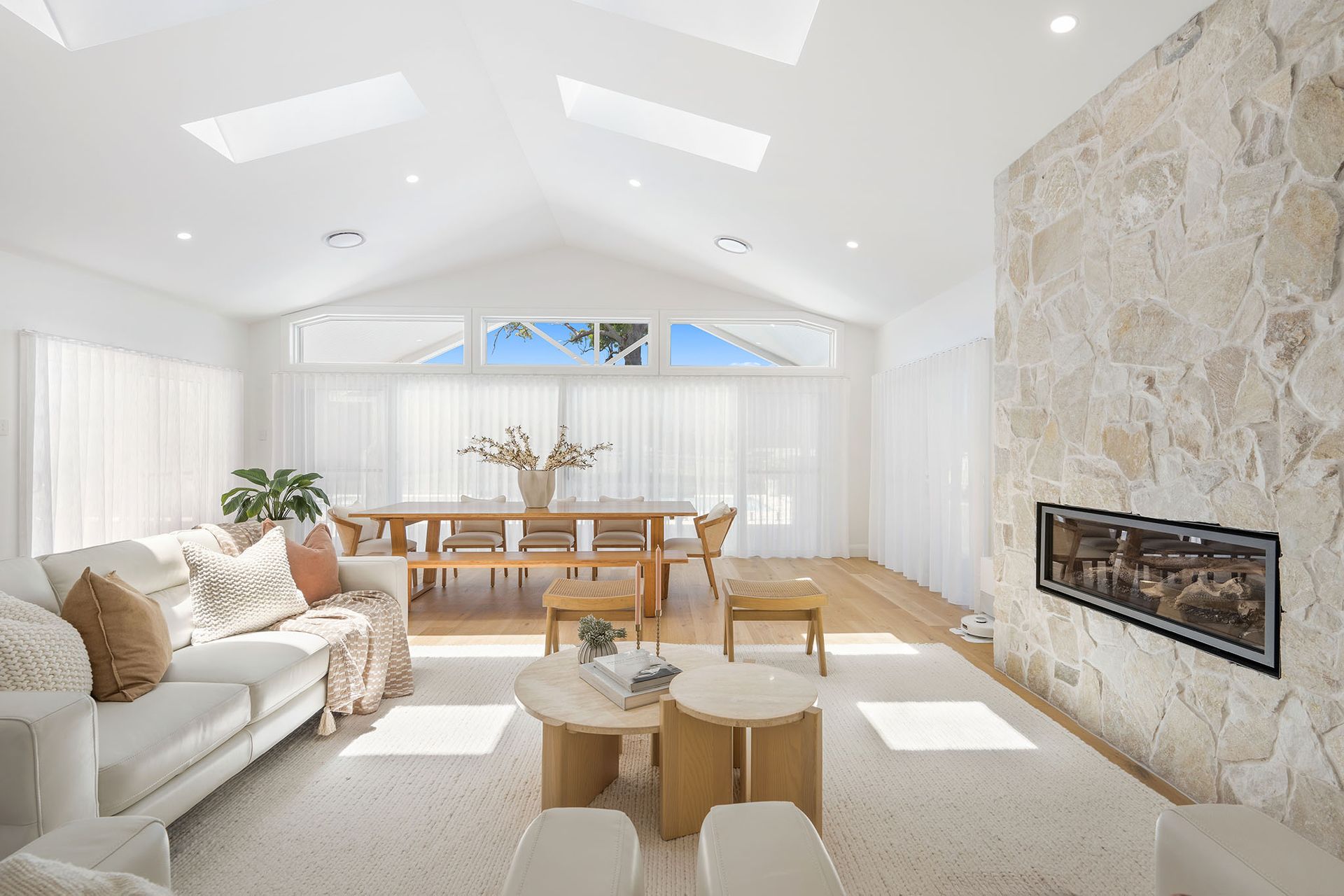 Bright, modern living room with stone fireplace, white sofa, and dining table in a sunlit open space