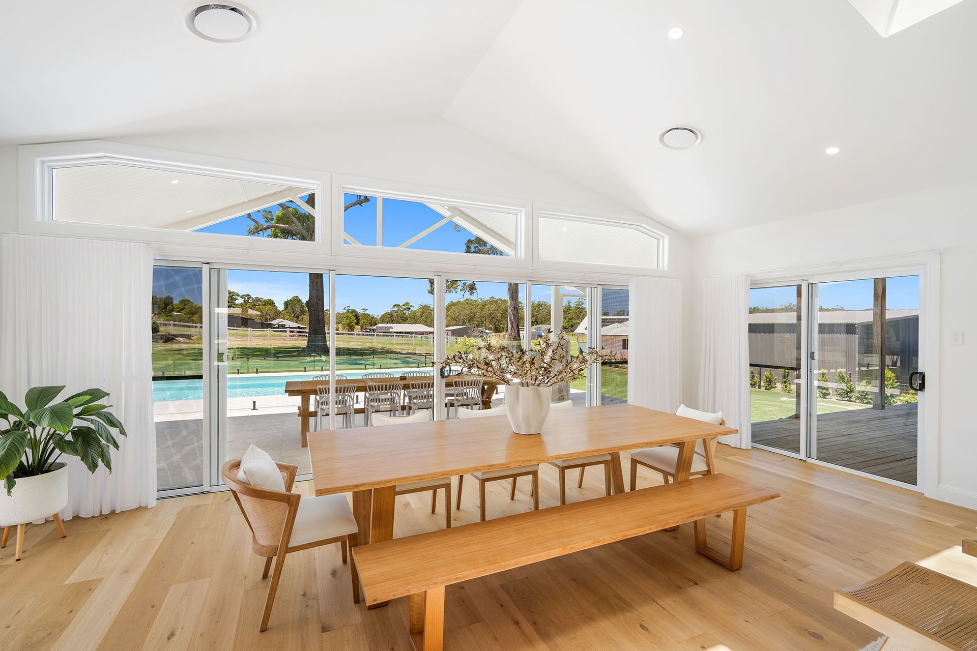 Bright dining room with a wooden table, large windows, and a view of a pool and ocean.