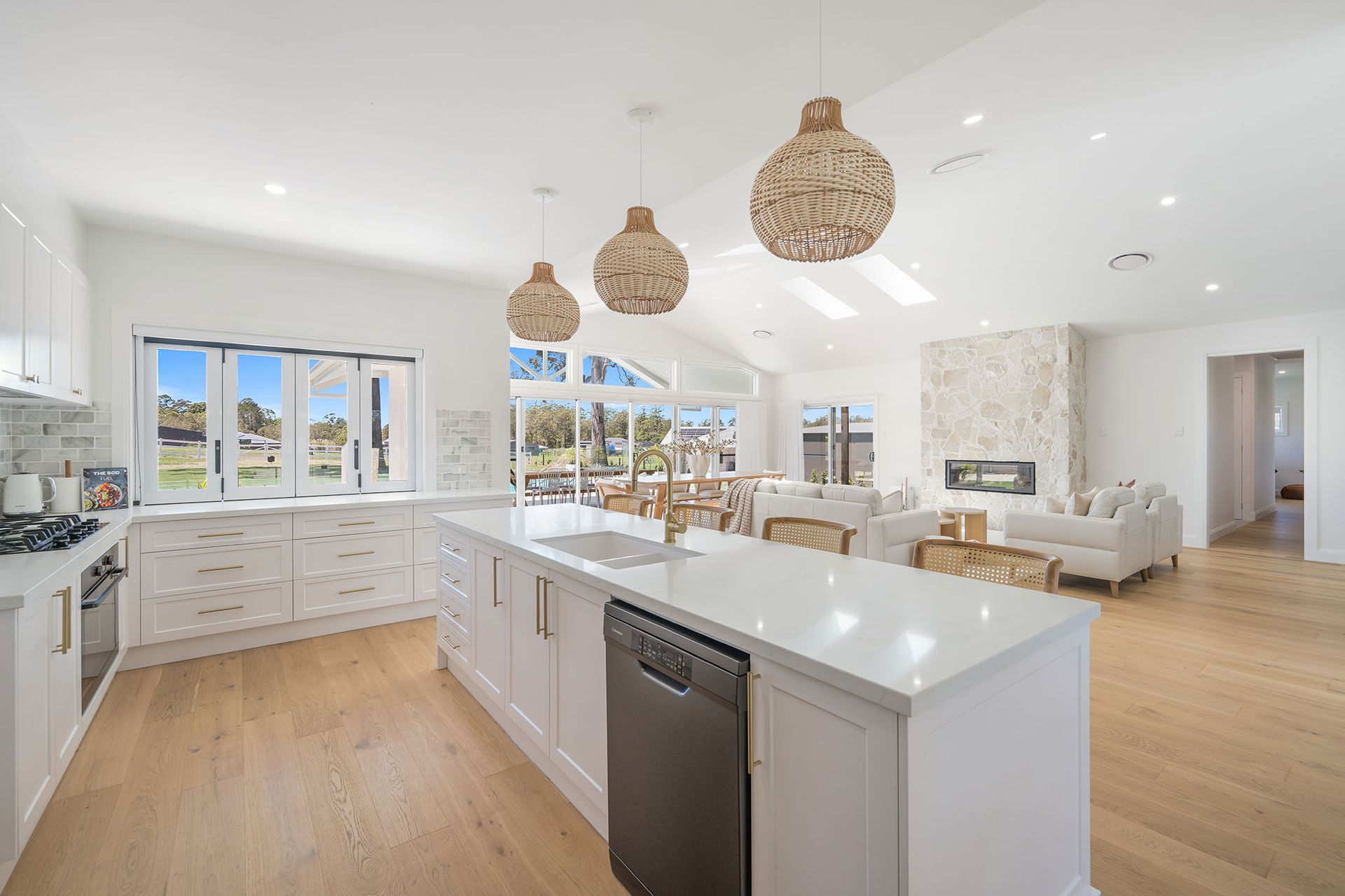 Bright modern kitchen with white cabinets, island, woven pendant lights, and hardwood floors