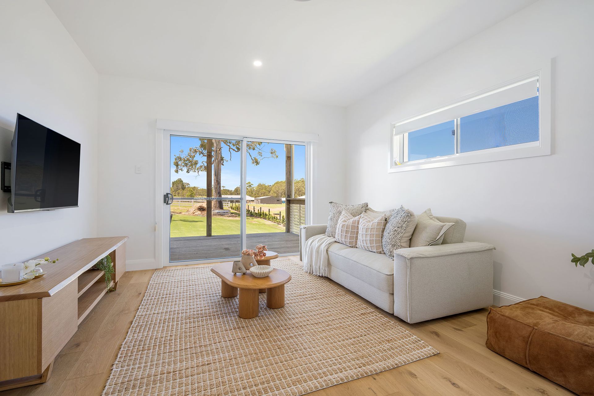 Bright living room with sofa, TV, coffee table, and sliding glass doors to a sunny backyard.