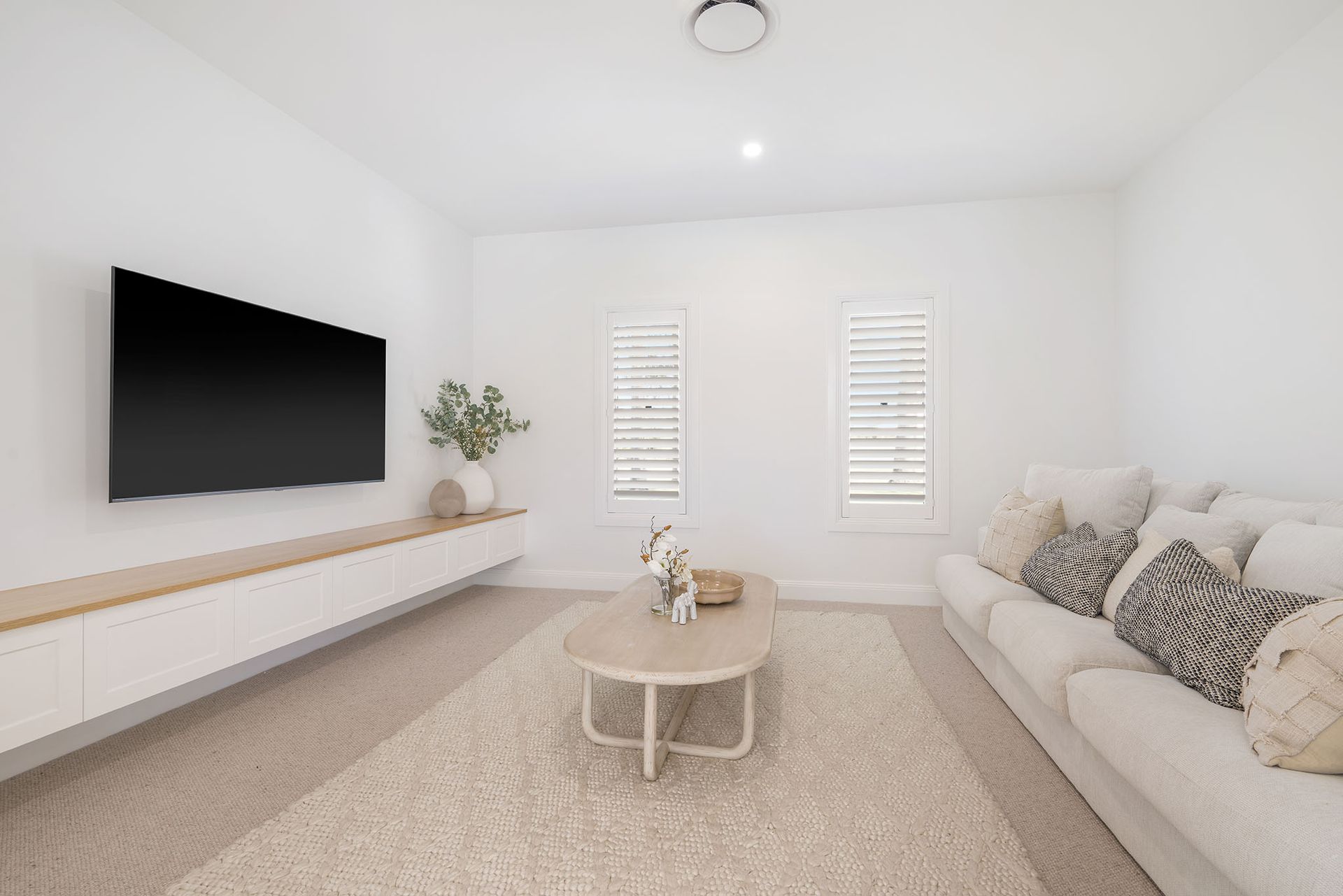 Minimal white living room with wall-mounted TV, beige sofa, and round coffee table