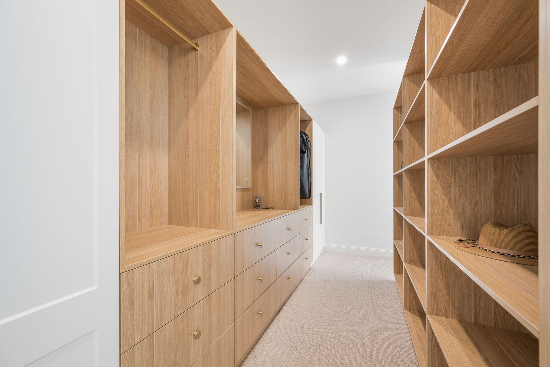 Modern hallway with light wood built-in cabinets and open shelving along a bright, carpeted corridor