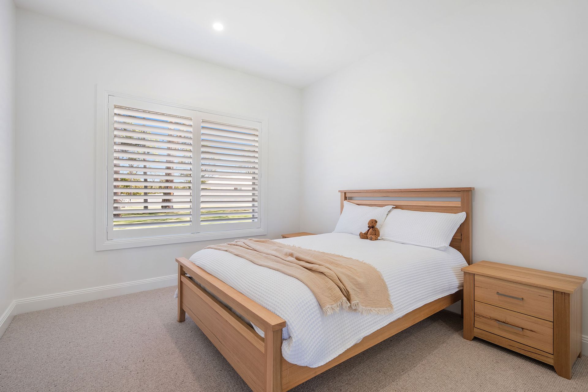 Bright bedroom with a wooden bed, white bedding, nightstand, and window blinds.