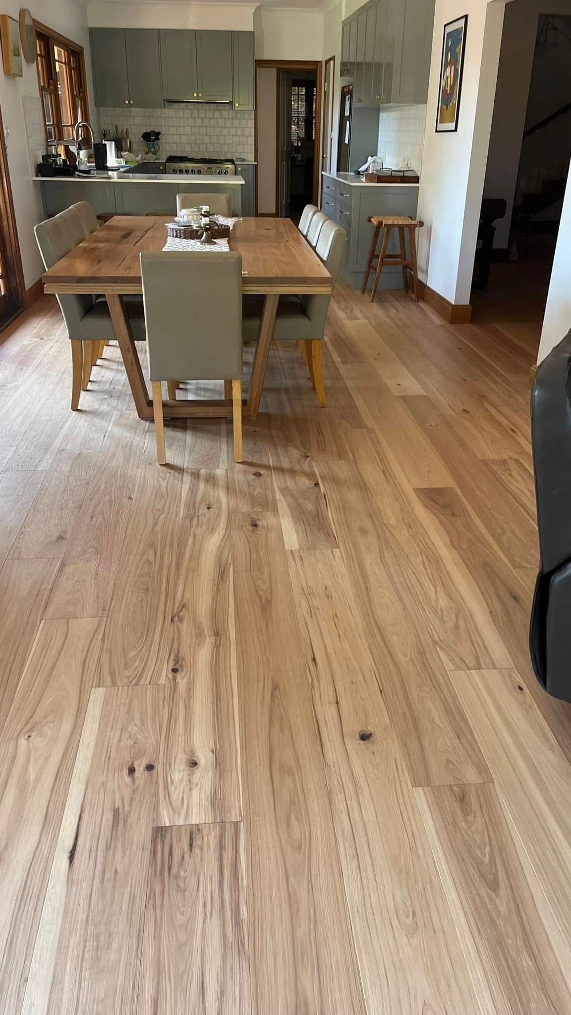 A dining table and chairs sit on wide-plank wood flooring in an open-concept kitchen with grey cabinets.