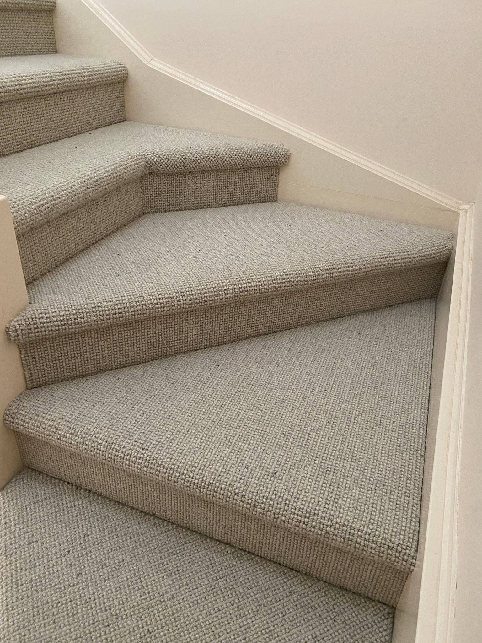 Carpeted stairs turning a corner, featuring light beige, textured wall-to-wall carpeting.