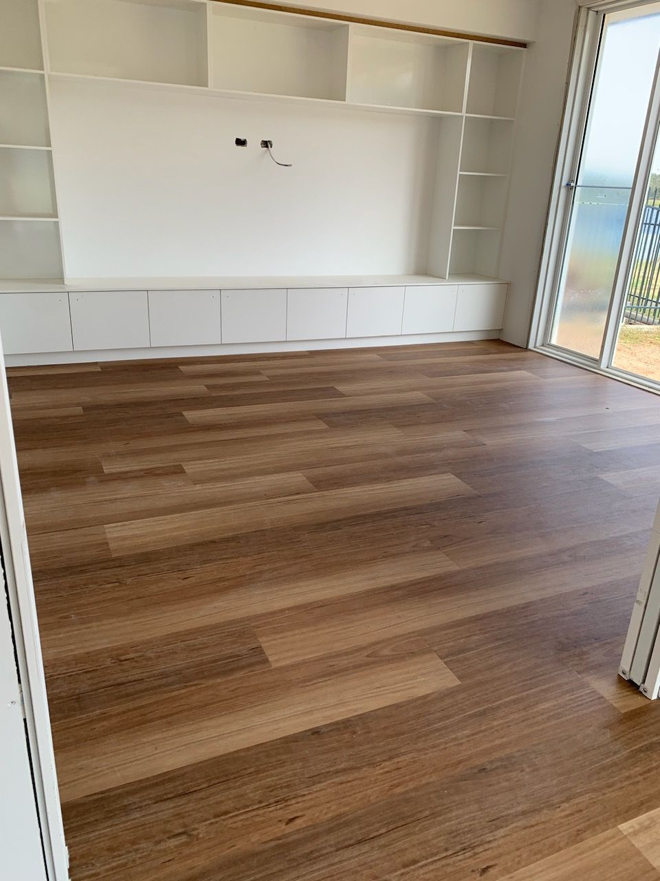 An Empty Living Room With Hardwood Floors And Sliding Glass Doors — Flooring Suppliers in Port Macquarie, NSW