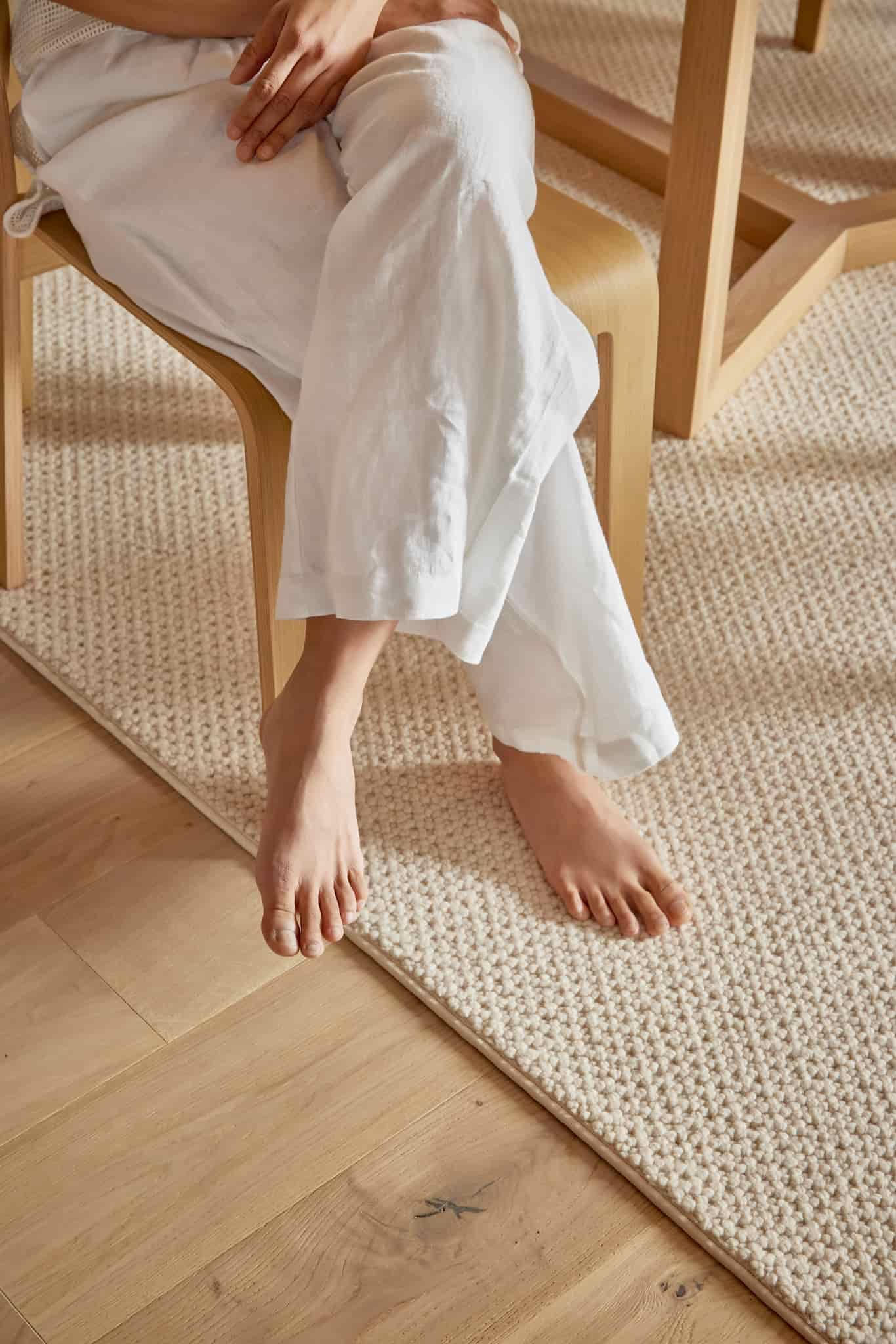 A Woman is Sitting on a Chair With Her Legs Crossed on a Rug — Flooring Suppliers in Port Macquarie, NSW