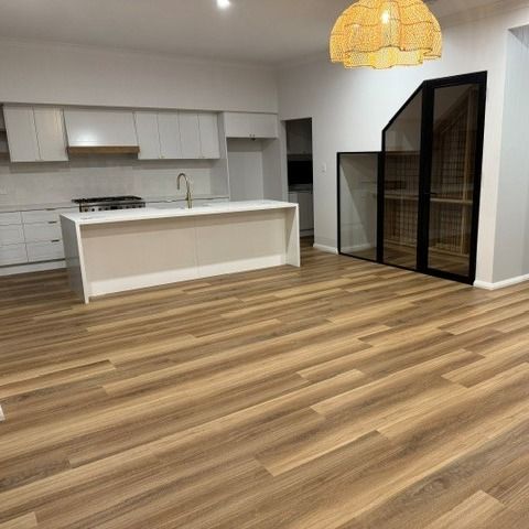 A modern kitchen featuring white cabinets, a large island, and a glass-enclosed wine storage area with wood flooring.