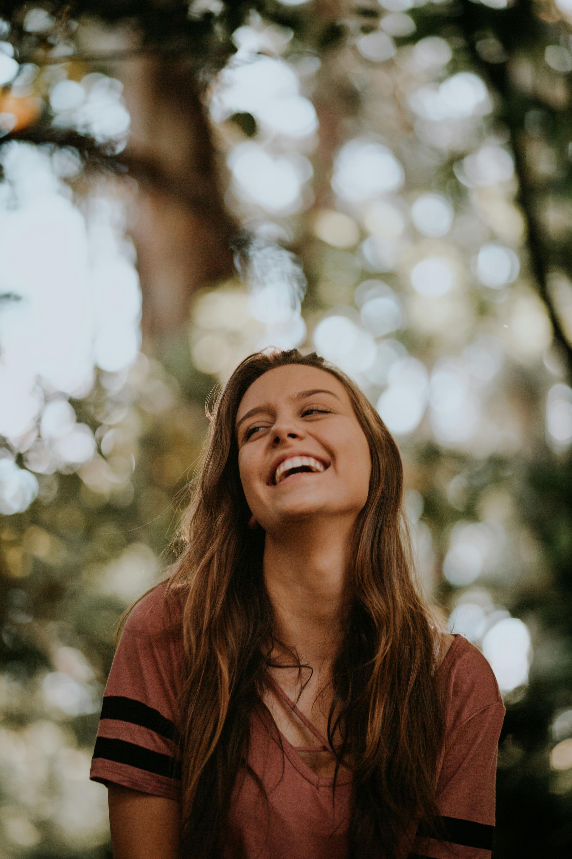 Smiling woman with long hair in a maroon shirt outdoors with blurred trees in the background
