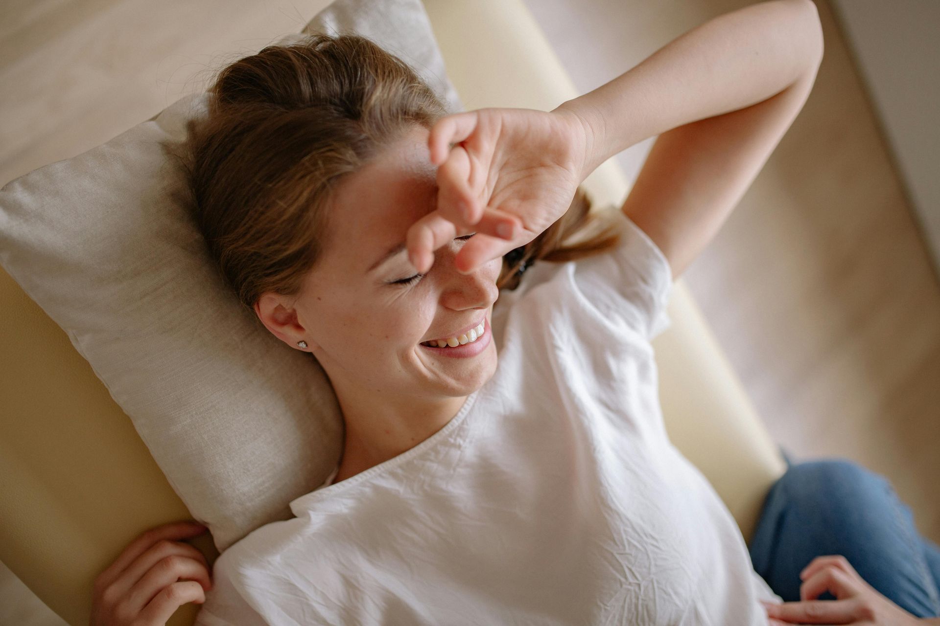 Woman lying on a bed, smiling and rubbing her eye with one hand