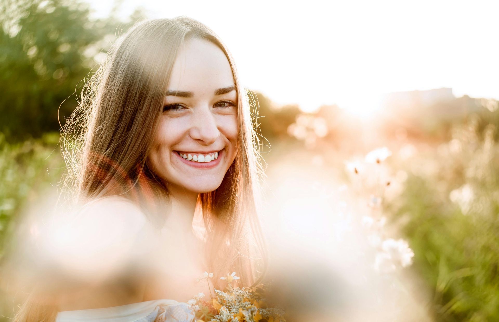 Smiling person in a sunlit field with soft, blurred flowers in the foreground