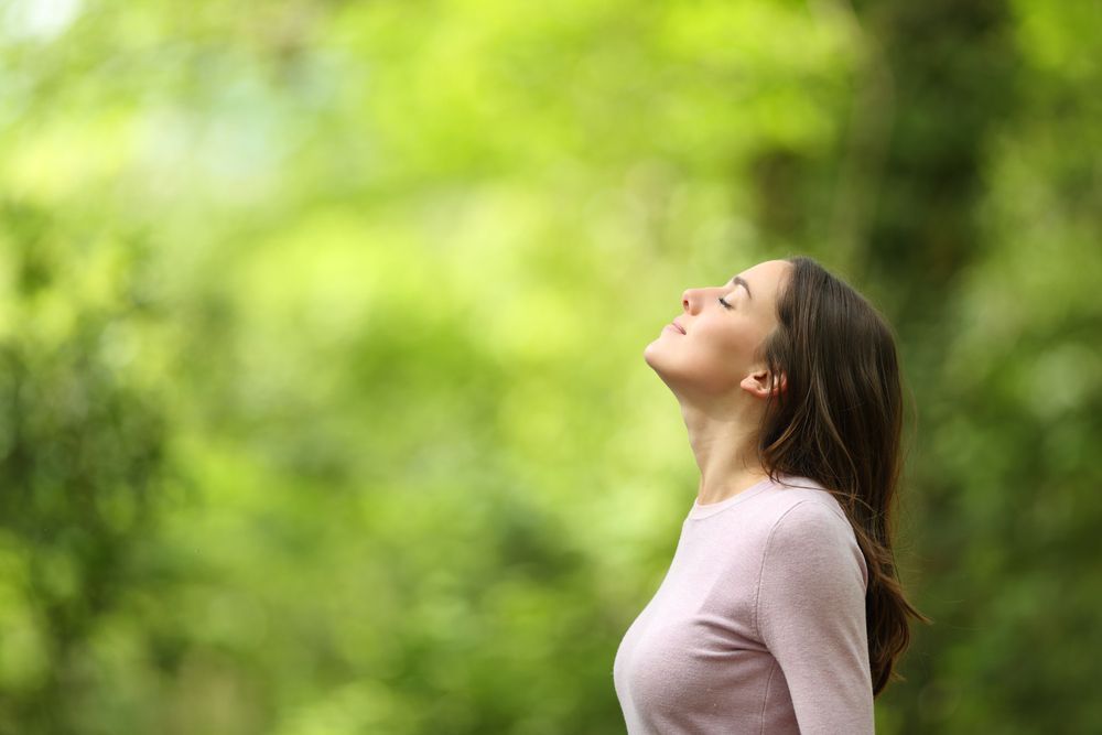 Smiling woman with long hair outdoors, looking up against a blurred tree background